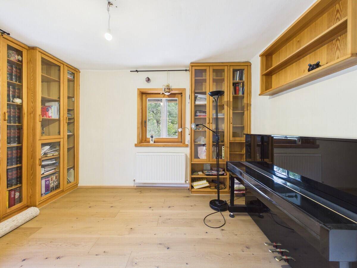 Geräumiges Wohnzimmer mit Holzparkett, Bücherregalen und einem schwarzen Flügel.
