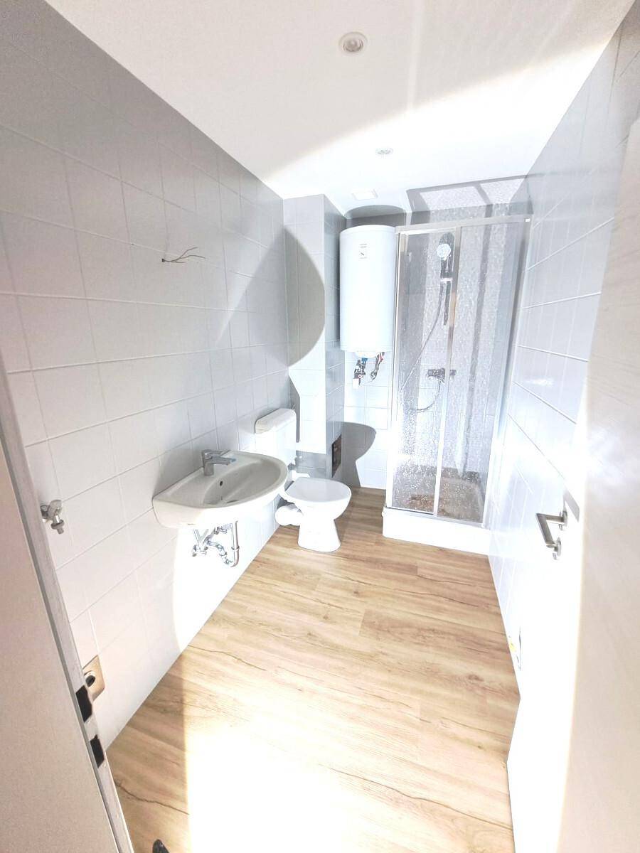 Funktionales Badezimmer mit Dusche, WC, Waschbecken und Warmwasserboiler.