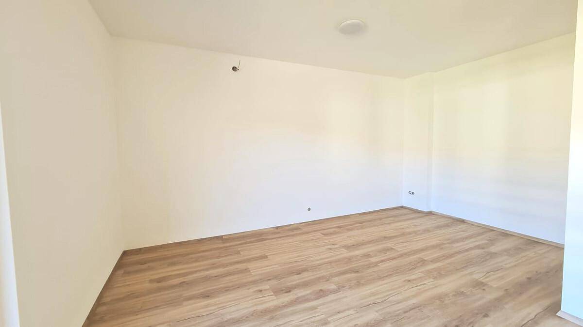 Heller, leerer Raum mit weißen Wänden und neuem Laminatboden.