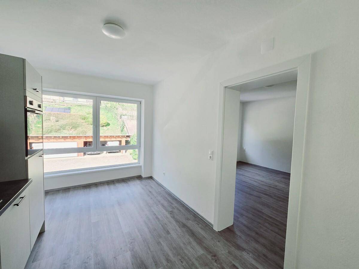 Heller Wohnbereich mit modernem Laminatboden und großem Fenster mit Ausblick ins Grüne.