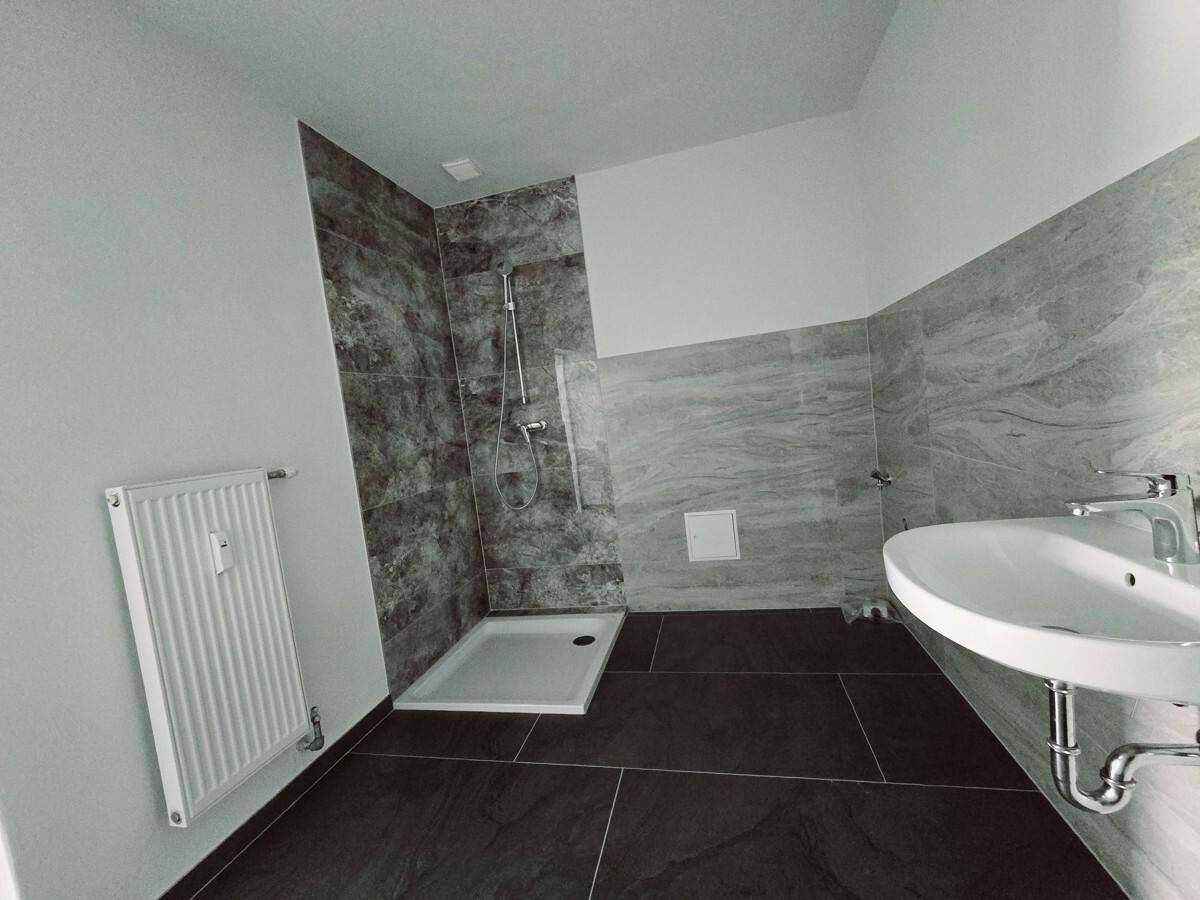 Geräumiges Badezimmer mit ebenerdiger Dusche, großem Waschbecken und modernen Fliesen.