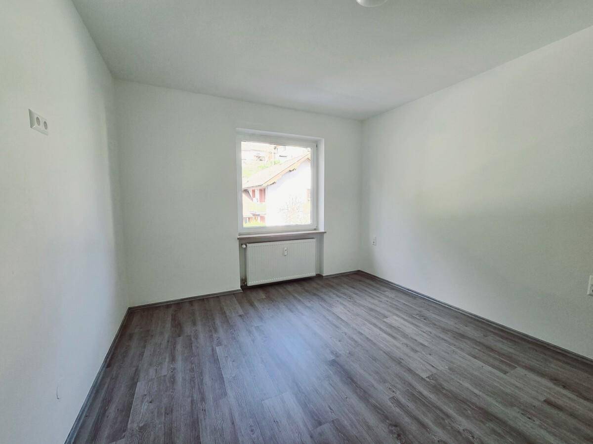 Helles Schlafzimmer mit dunklem Laminatboden und einem Fenster, das viel Tageslicht hereinlässt.