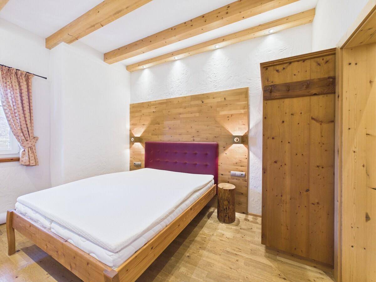 Gemütliches Schlafzimmer mit Holzbalkendecke, Holzwand und modernem Doppelbett.