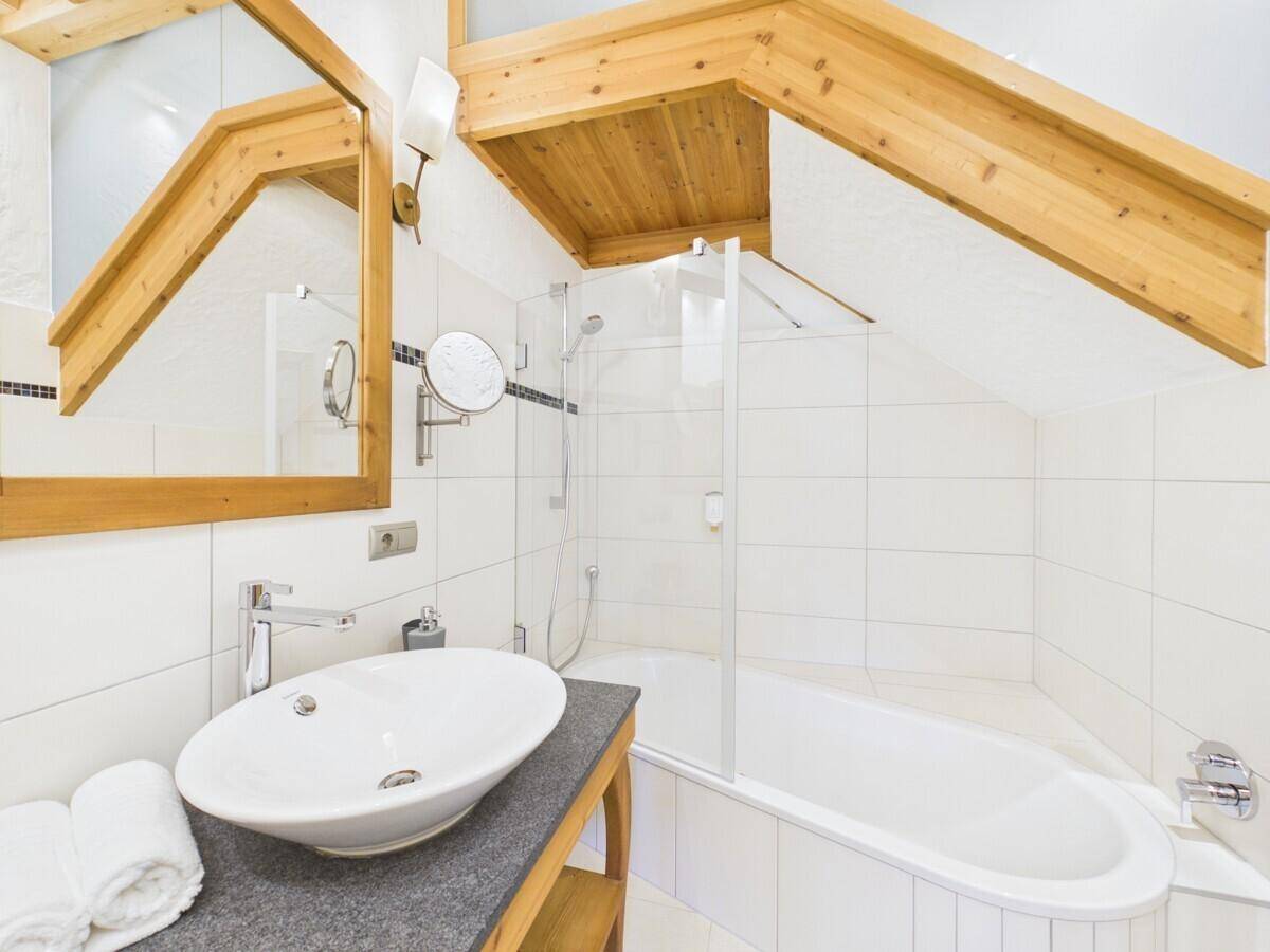 Helles Badezimmer mit ovalem Waschbecken, Spiegel und Badewanne unter Holzbalken.