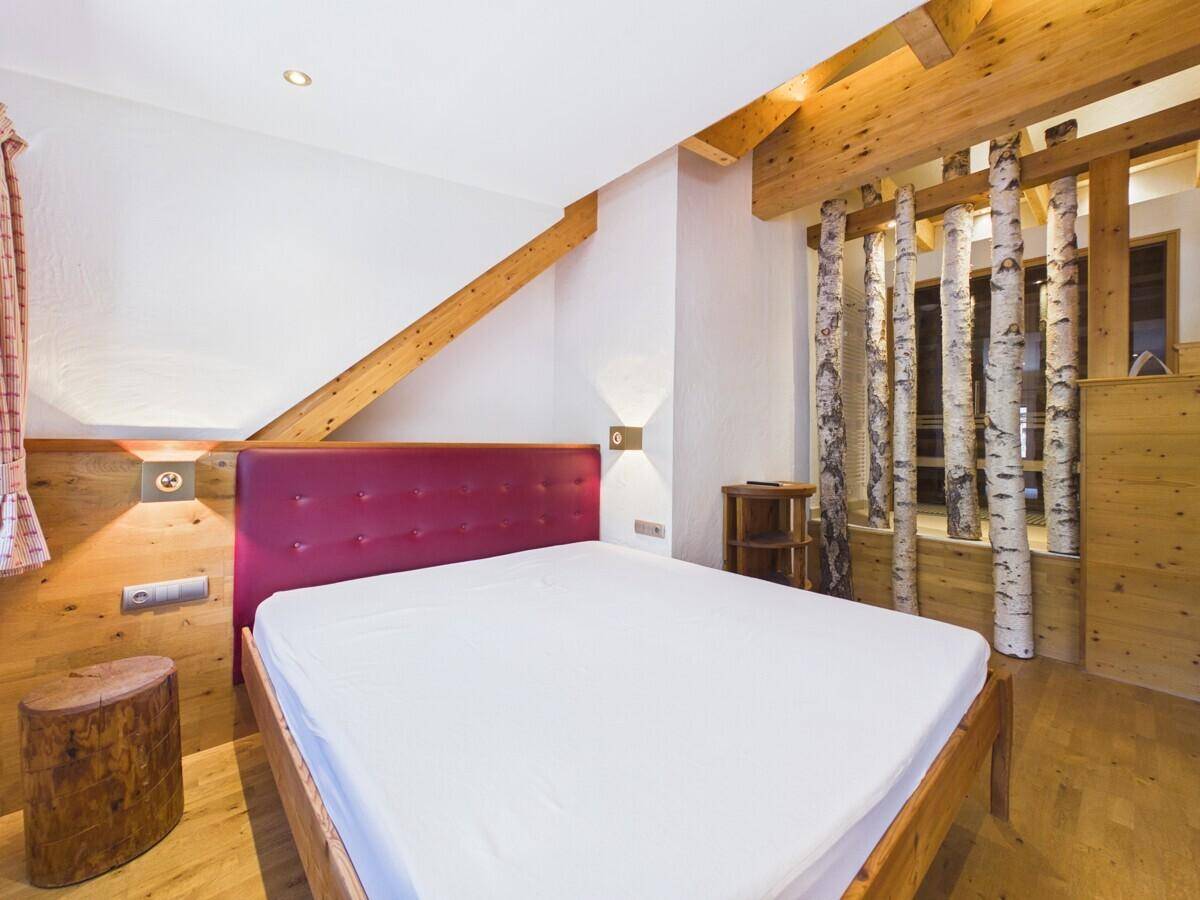 Gemütliches Schlafzimmer mit Doppelbett, Holzbalken und dekorativen Birkenstämmen.