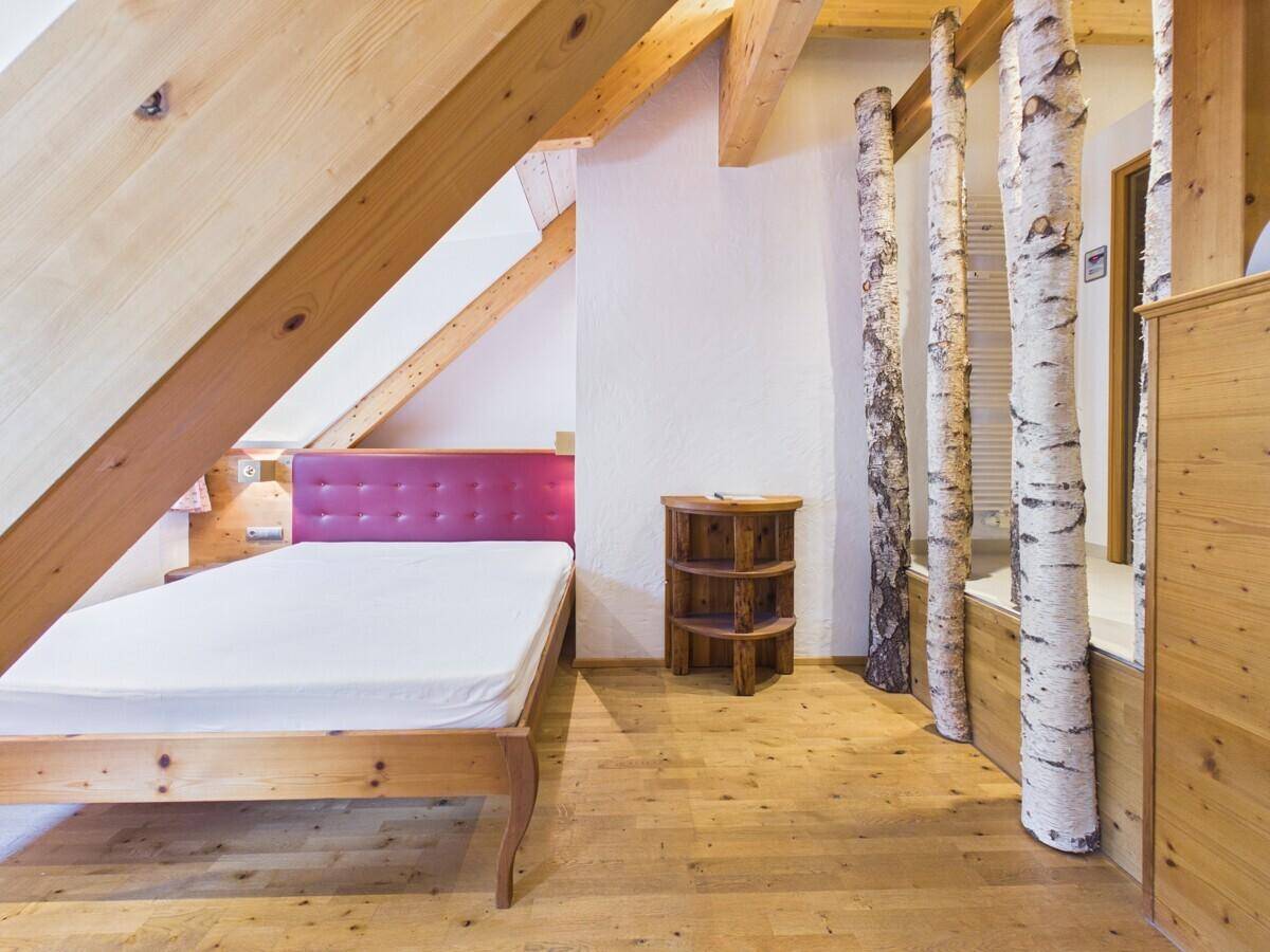 Schlafzimmer mit Holzboden, Holzbalken und dekorativen Birkenstämmen als Akzent.