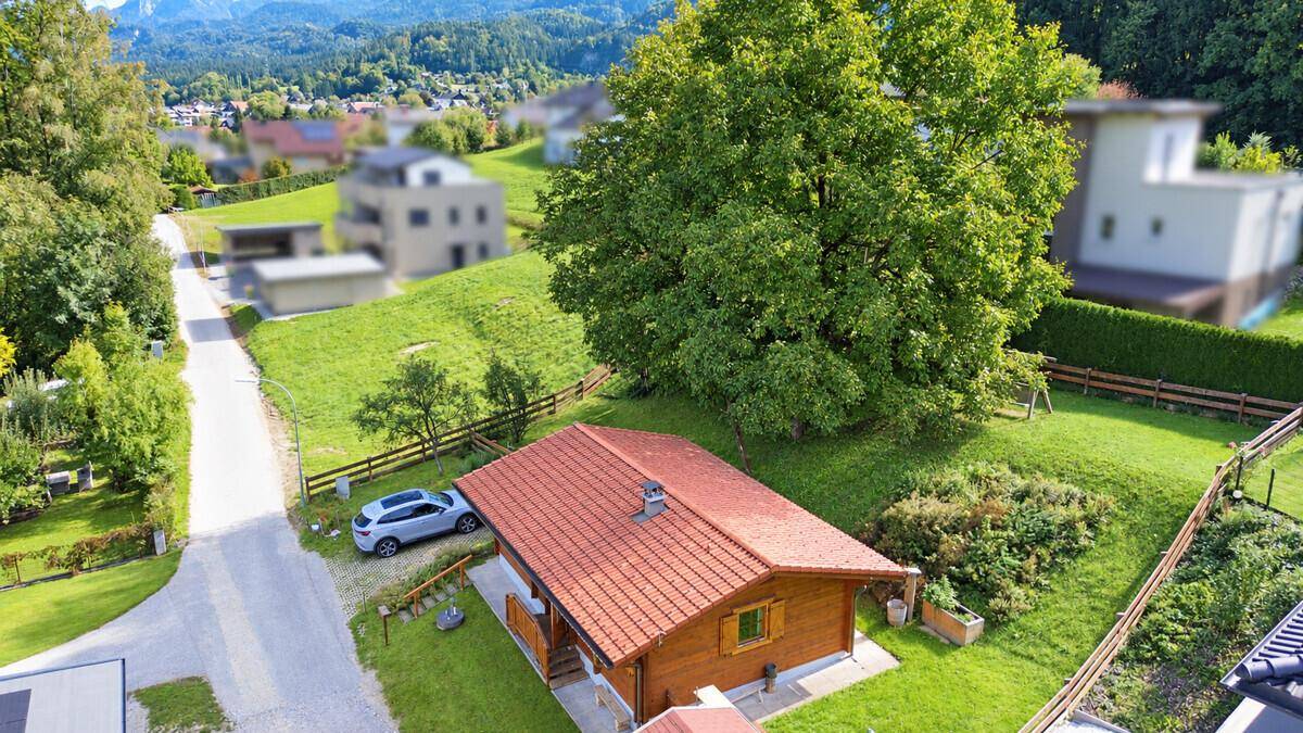 Draufsicht auf ein Holzhaus mit rotem Ziegeldach, umgeben von grünen Hügeln und Bäumen.