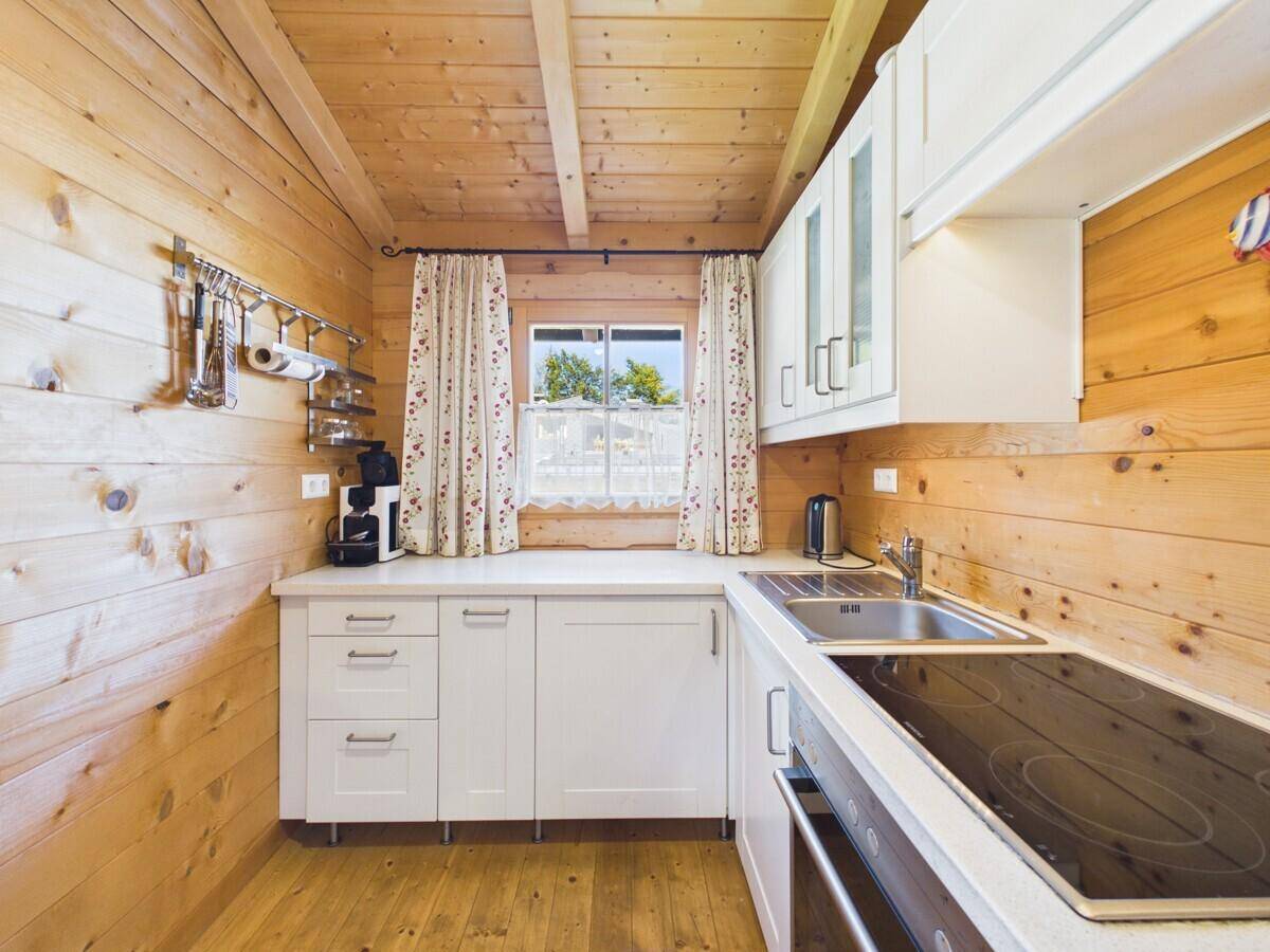 Kleine Küche mit weißen Schränken, Kochfeld und Fenster in einem rustikalen Holzinterieur.