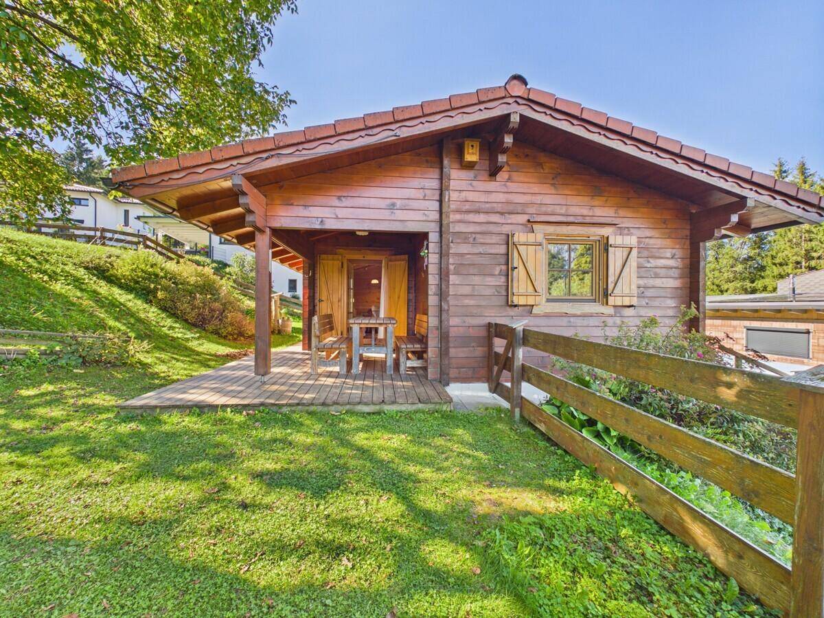Charmantes Holzchalet mit überdachter Terrasse, umgeben von einem gepflegten Rasen und Holzzaun.