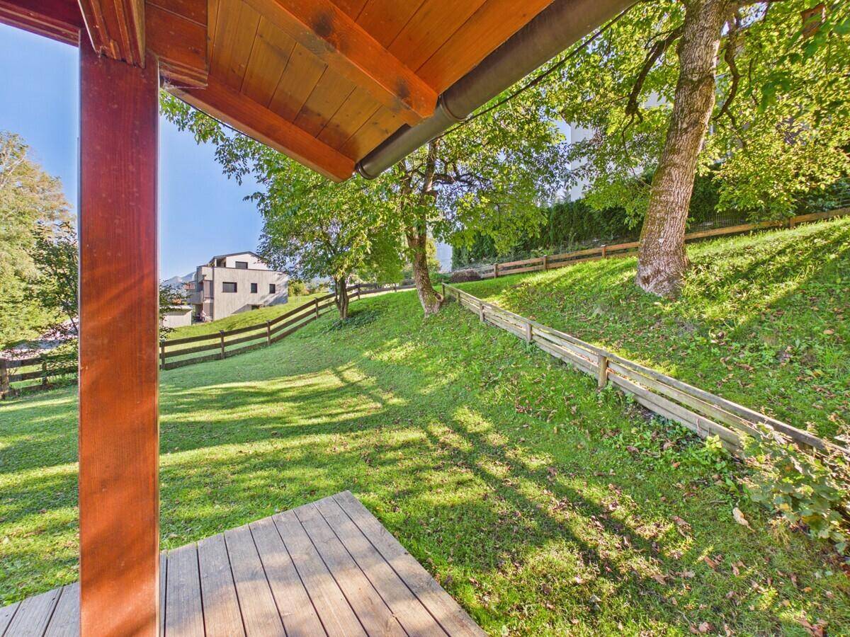 Blick von der überdachten Holzterrasse auf die grüne Wiese und die umliegende Natur mit Bäumen.