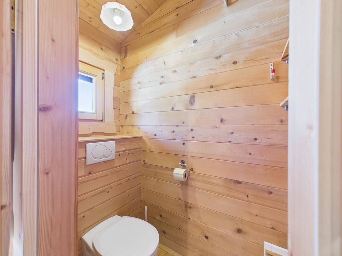 Separates WC mit Holzwänden, wandhängender Toilette und kleinem Fenster.