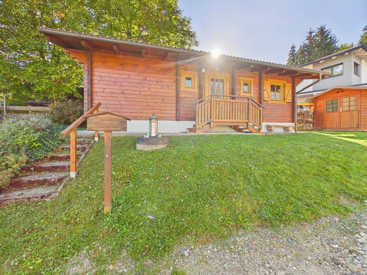 Holzchalet mit Eingangsbereich, einem kleinen Holzschild und gepflegtem Rasen unter strahlendem Himmel.