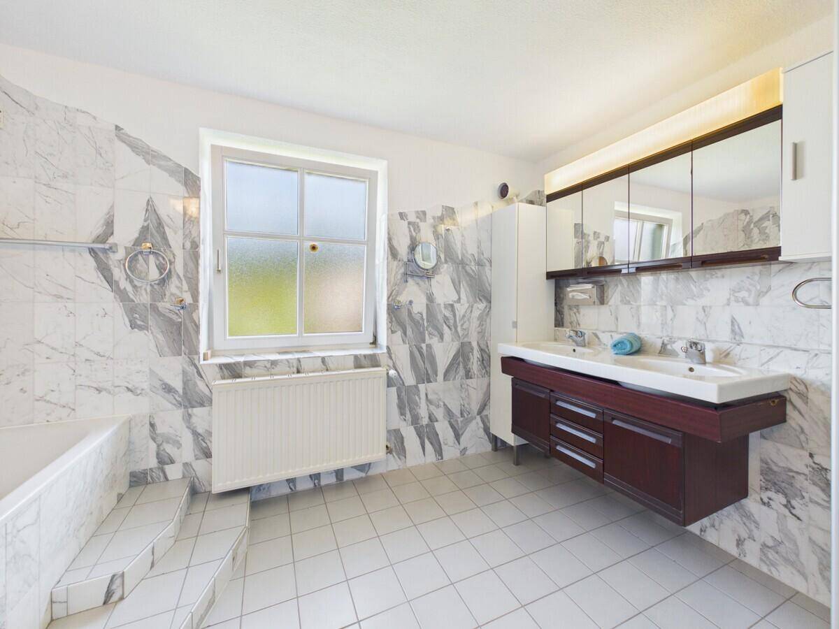 Geräumiges Badezimmer mit Marmorfliesen, Doppelwaschbecken und Badewanne mit Stufen.
