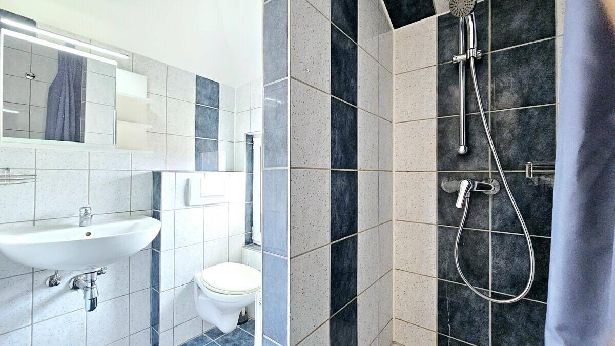 Badezimmer mit Fliesen, Waschbecken, Toilette und Duschbereich mit Vorhang.
