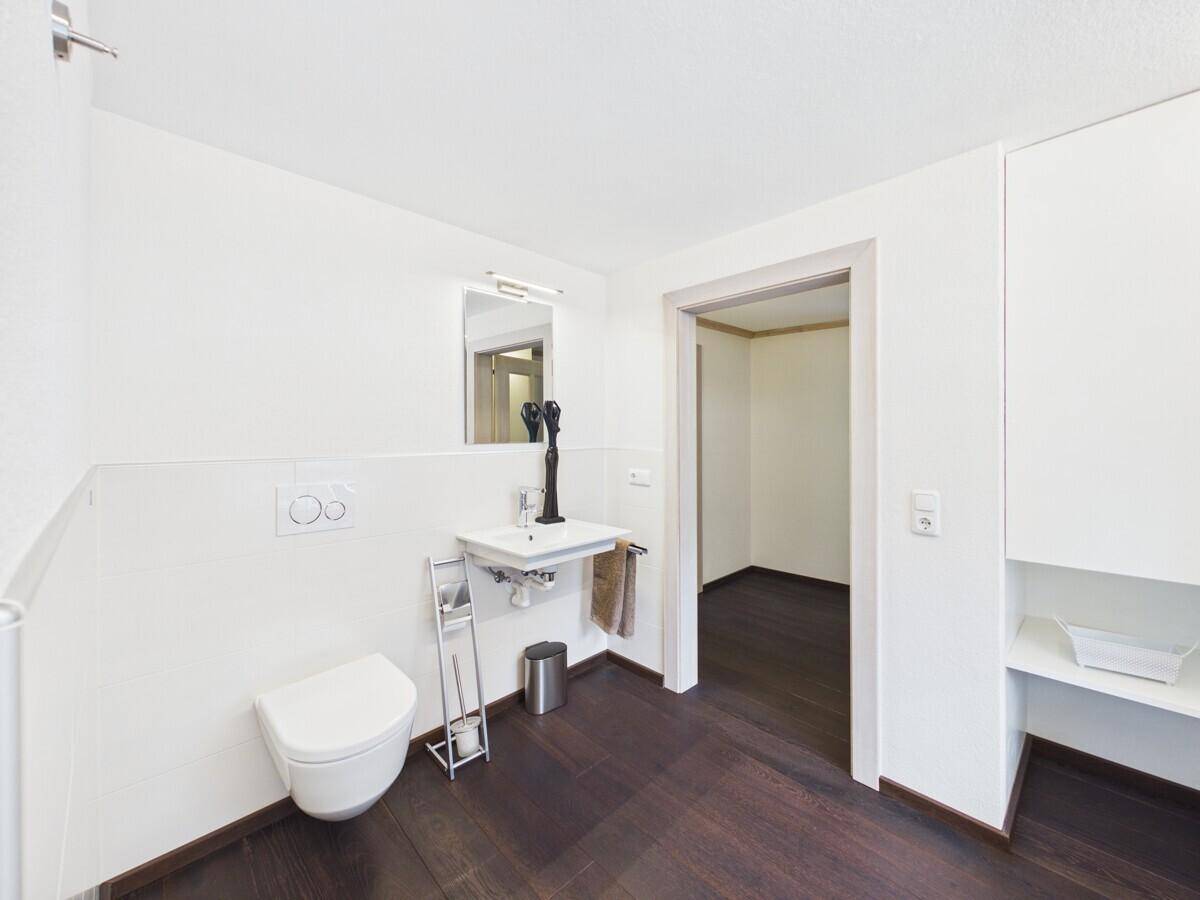 Helles Badezimmer mit Einzelwaschbecken, wandhängendem WC und dunklem Holzboden.