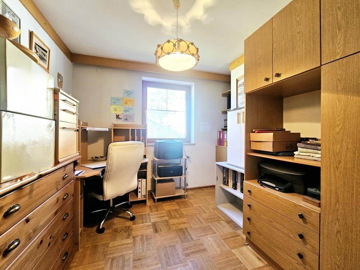 Helles Arbeitszimmer mit Parkettboden, Holzmöbeln und Blick nach draußen.