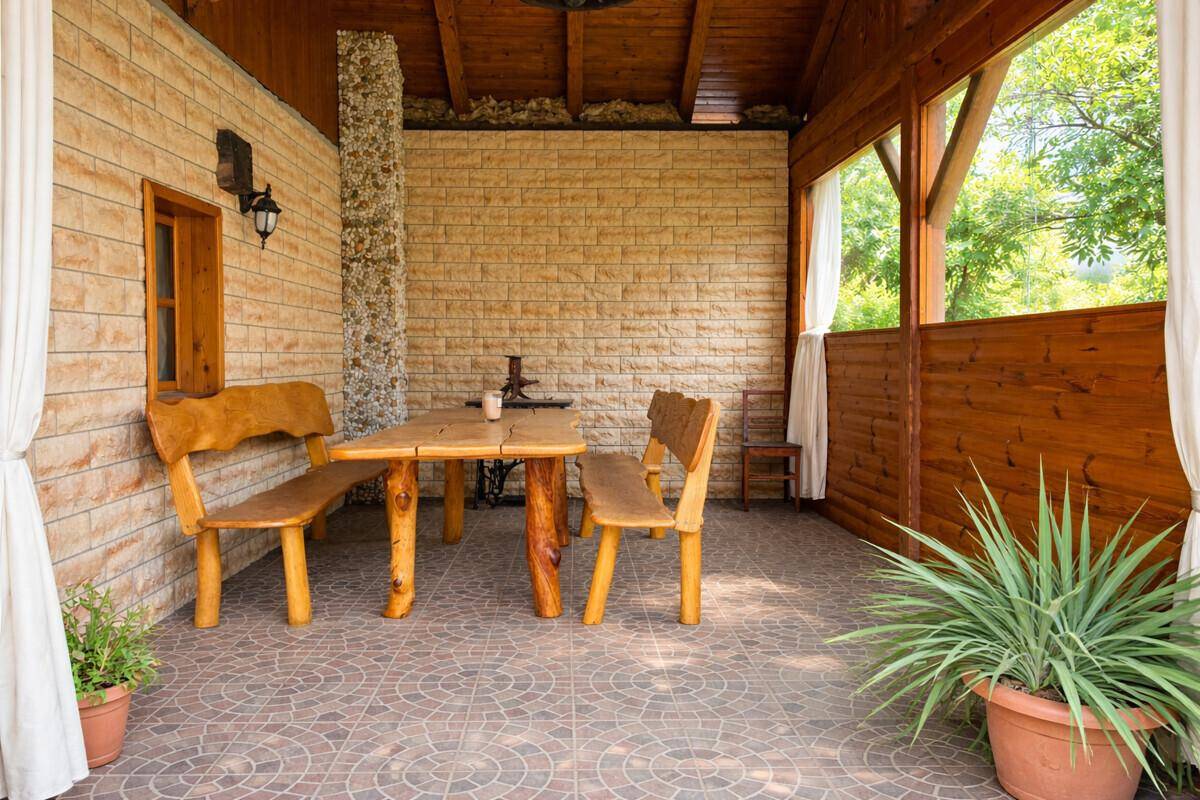 Detailansicht der überdachten Terrasse mit rustikalen Holzmöbeln und Fliesenboden.