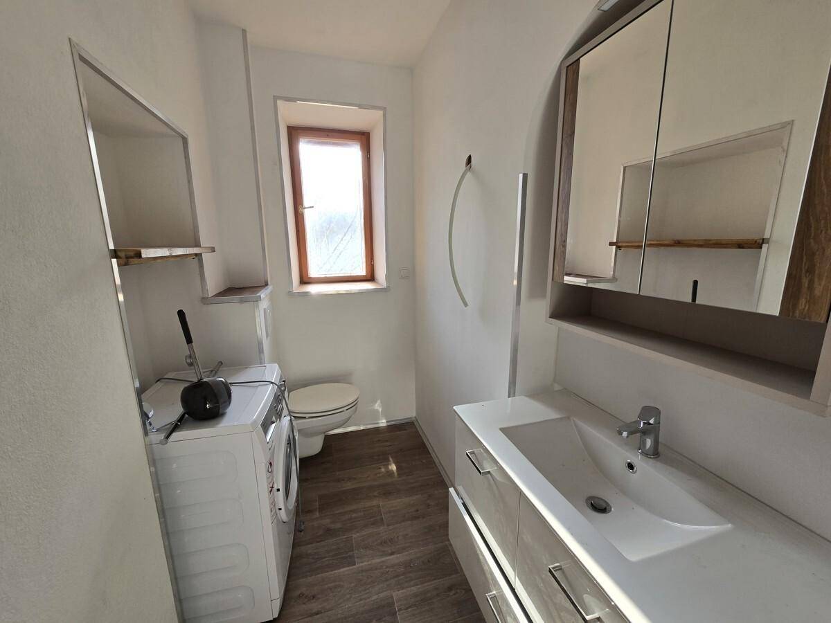 Helles Badezimmer mit Waschtisch, Spiegelschrank und Fenster, inklusive Waschmaschine für Komfort.
