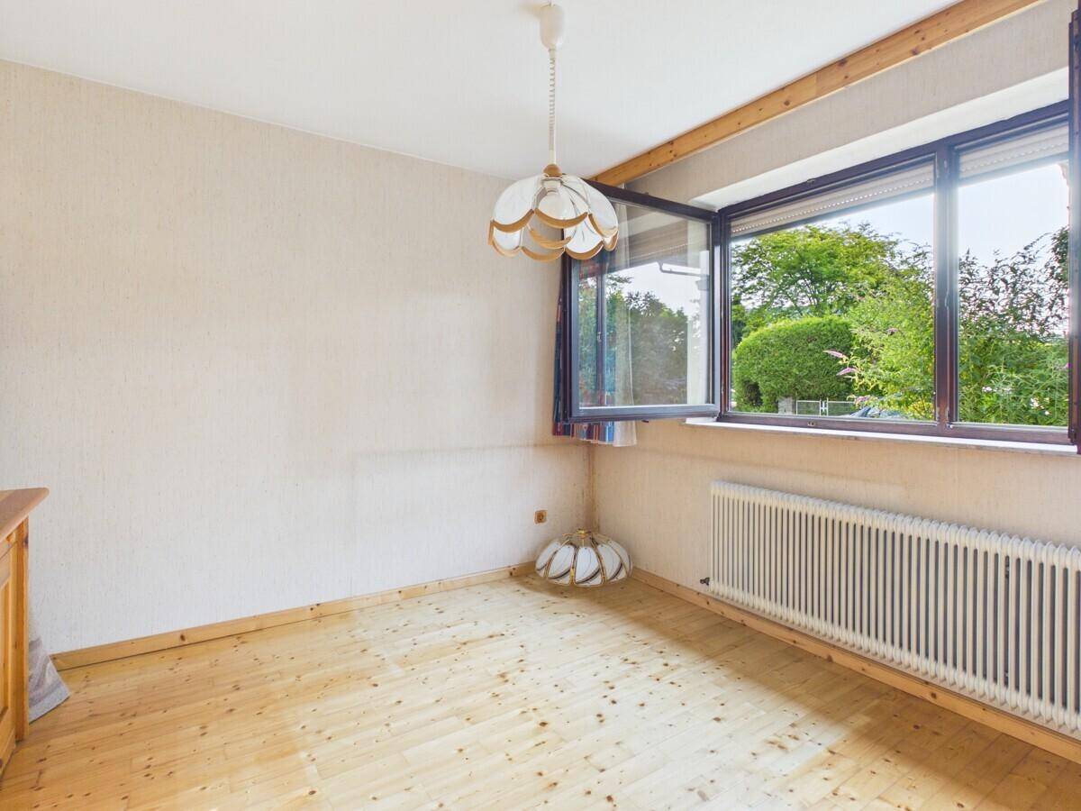 Helles Zimmer mit Holzboden, großer Fensterfront und Blick auf die grüne Umgebung.