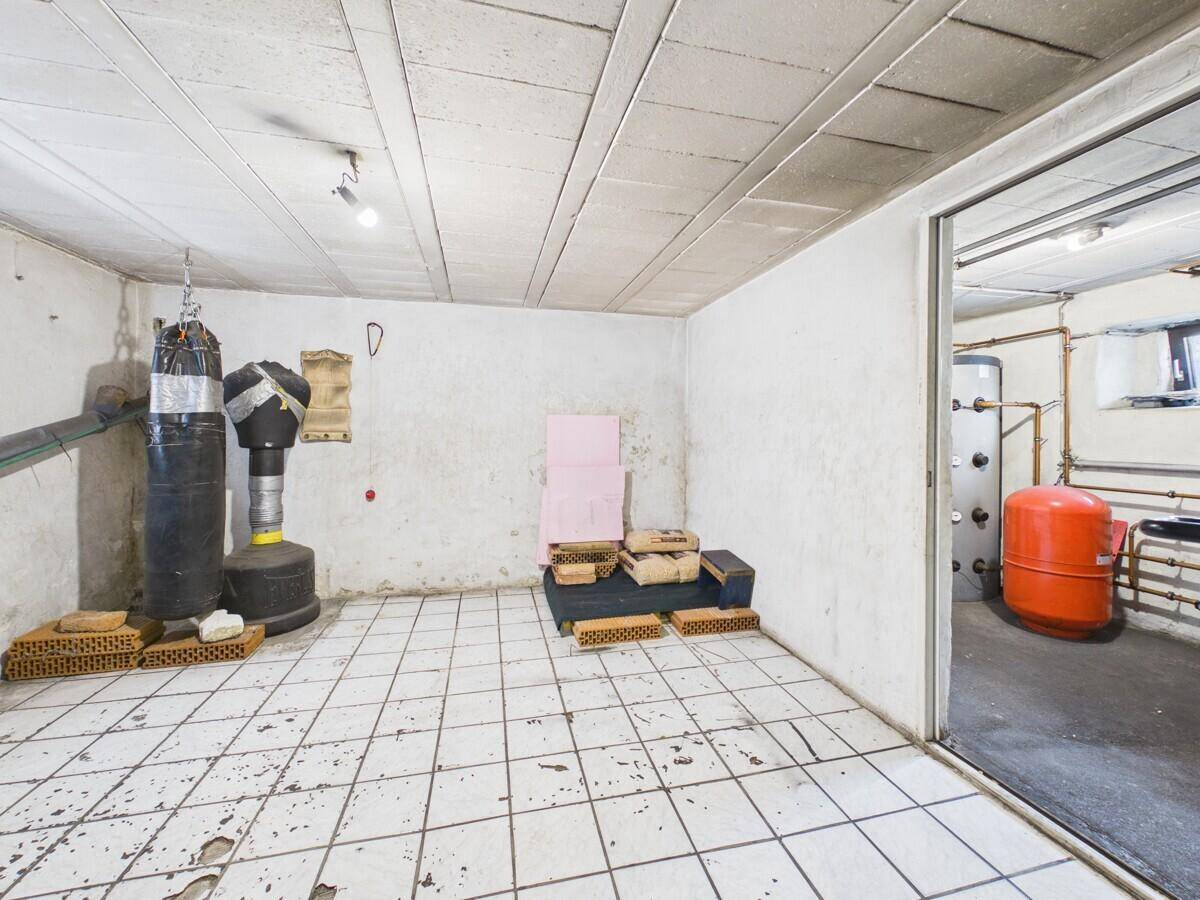 Kellerraum mit Fliesenboden, Boxsack und Blick in einen Heizungsraum mit technischen Anlagen.