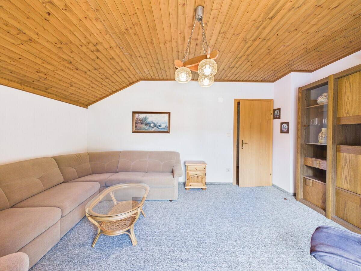 Geräumiges Wohnzimmer im Dachgeschoss mit Holzdecke, Teppichboden und gemütlicher Sitzecke.