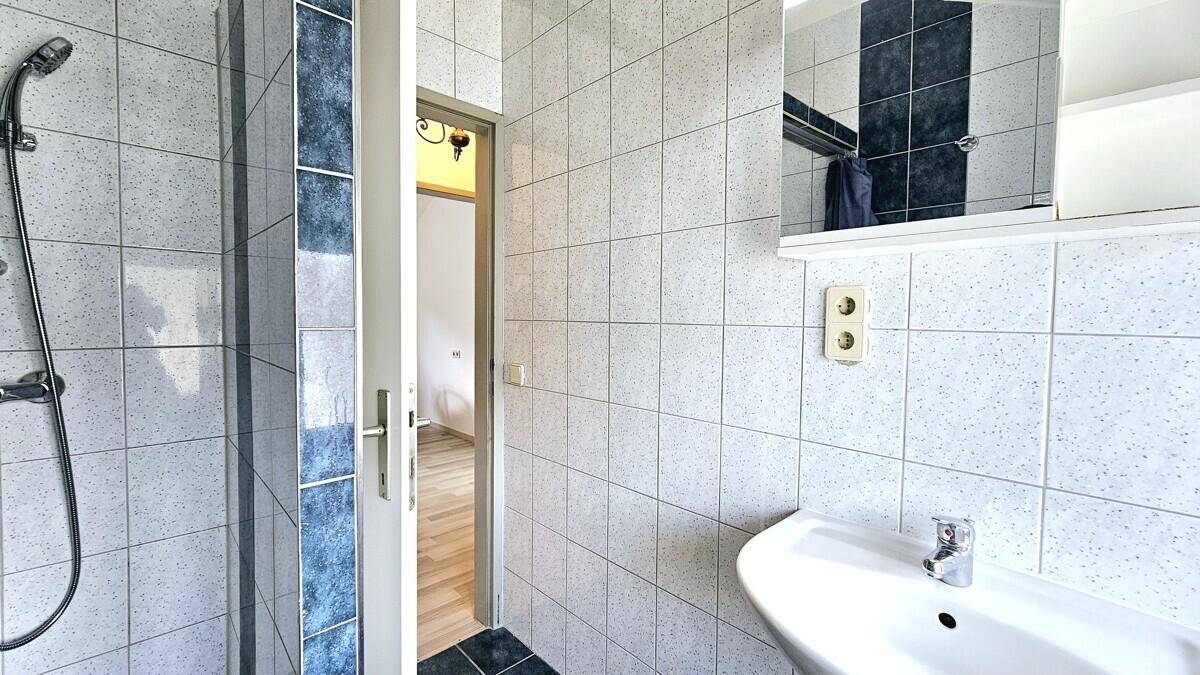 Badezimmer mit Waschbecken, Spiegelschrank und Duschbereich, gekennzeichnet durch weiße und blaue Fliesen.
