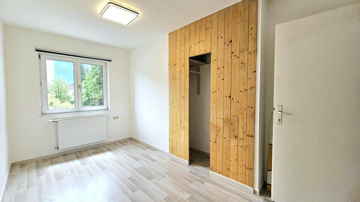 Schlafzimmer mit Laminatboden, Fenster und Holzwand mit integriertem Kleiderschrank.