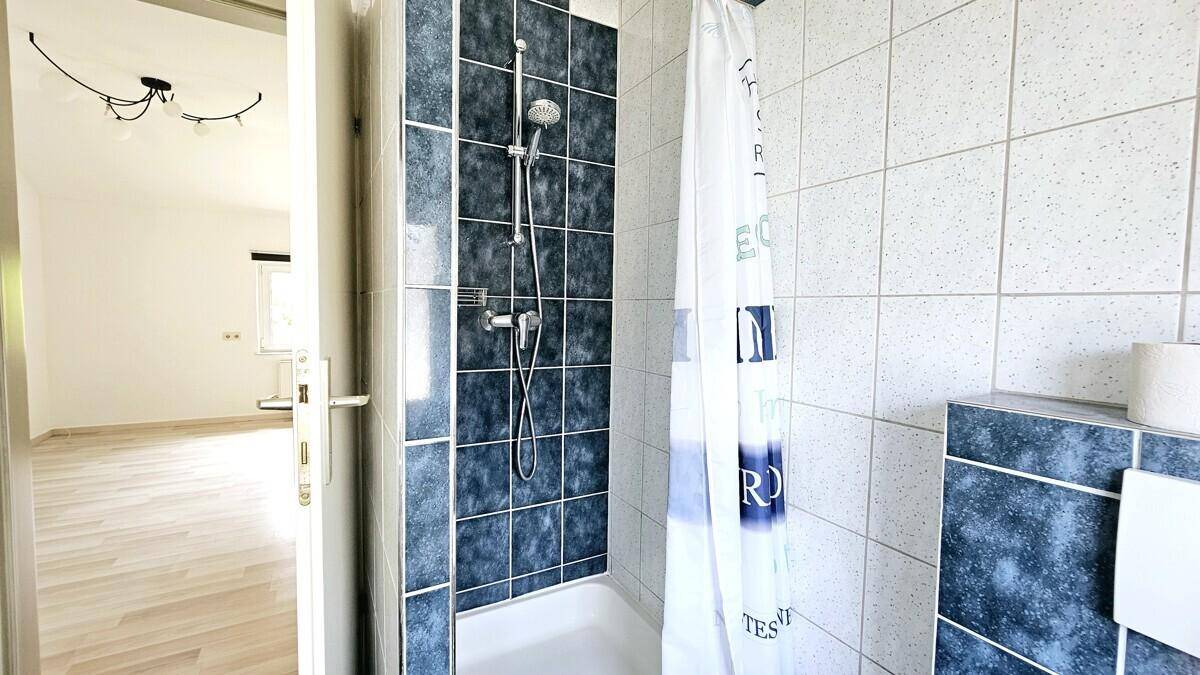 Badezimmer mit Duschbereich und hellen Fliesen, die einen Kontrast zu den dunkleren Akzenten bilden.