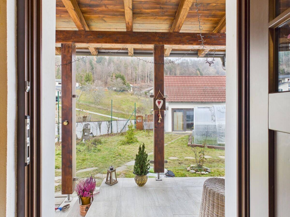 Überdachte Loggia mit Holzbalken und Blick auf den Garten und die umliegende Landschaft.
