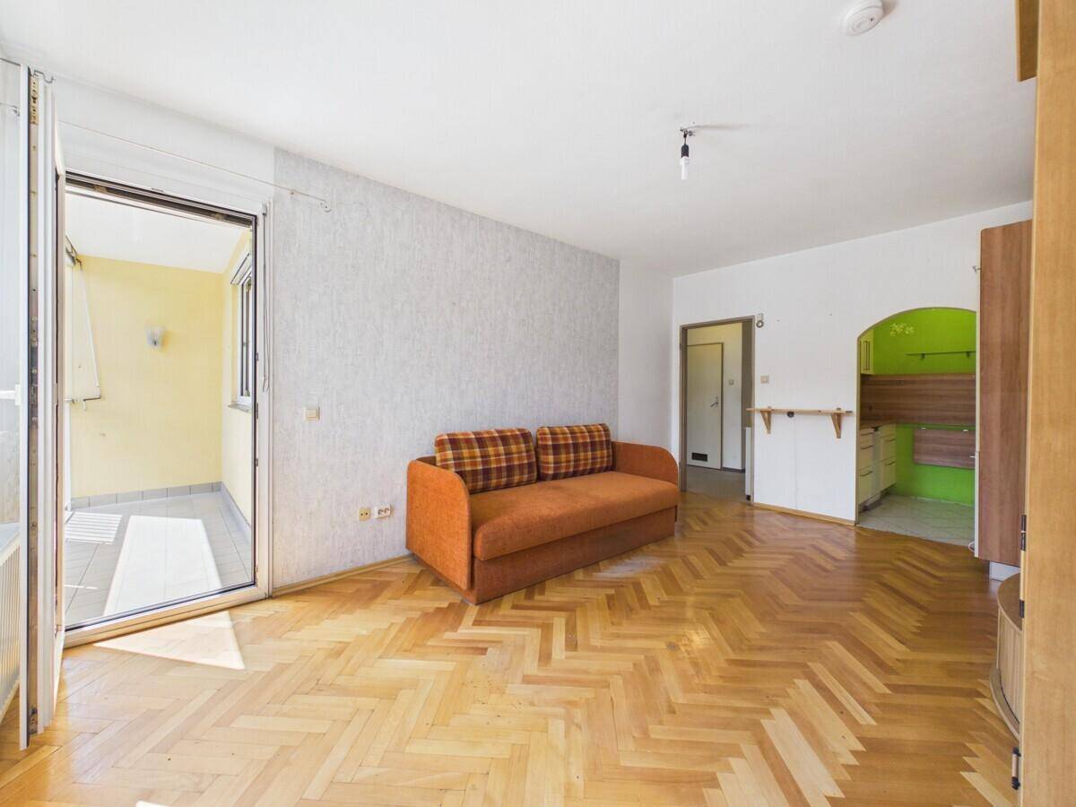 Wohnzimmer mit Fischgrätparkett, orangefarbenem Sofa und direktem Zugang zum Balkon.