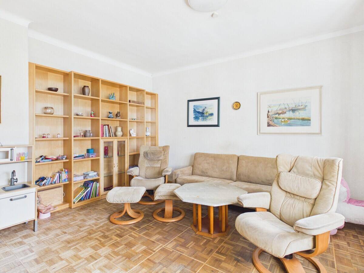 Gemütliches Wohnzimmer mit Holzbücherregal, bequemen Sesseln und Parkettboden.