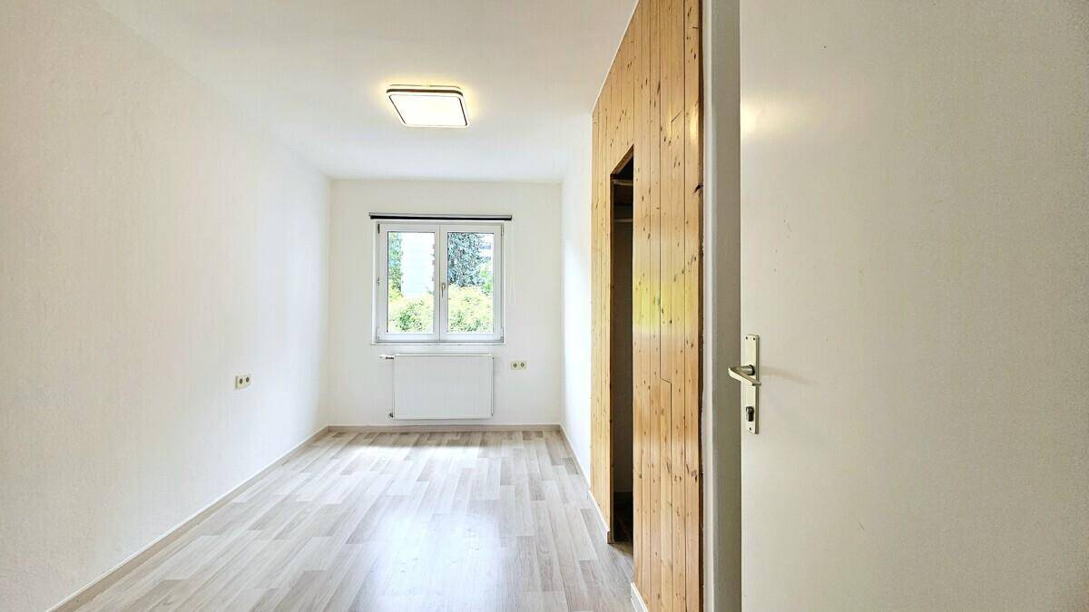 Geräumiges Schlafzimmer mit Laminatboden und Holzwand mit praktischer Schranknische.