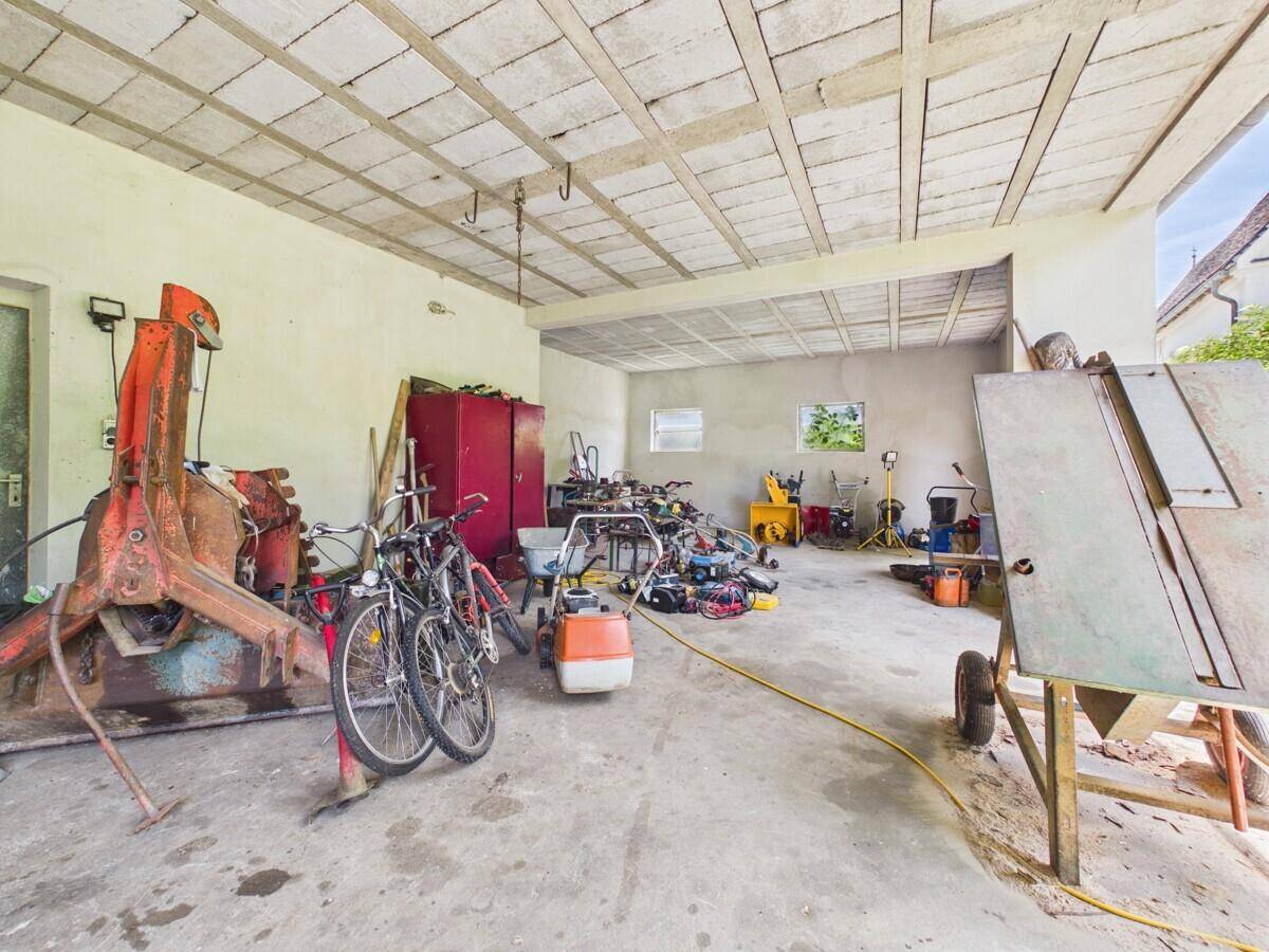 Geräumige Garage oder Werkstatt mit Betonboden, Fahrrädern und verschiedenen Geräten.