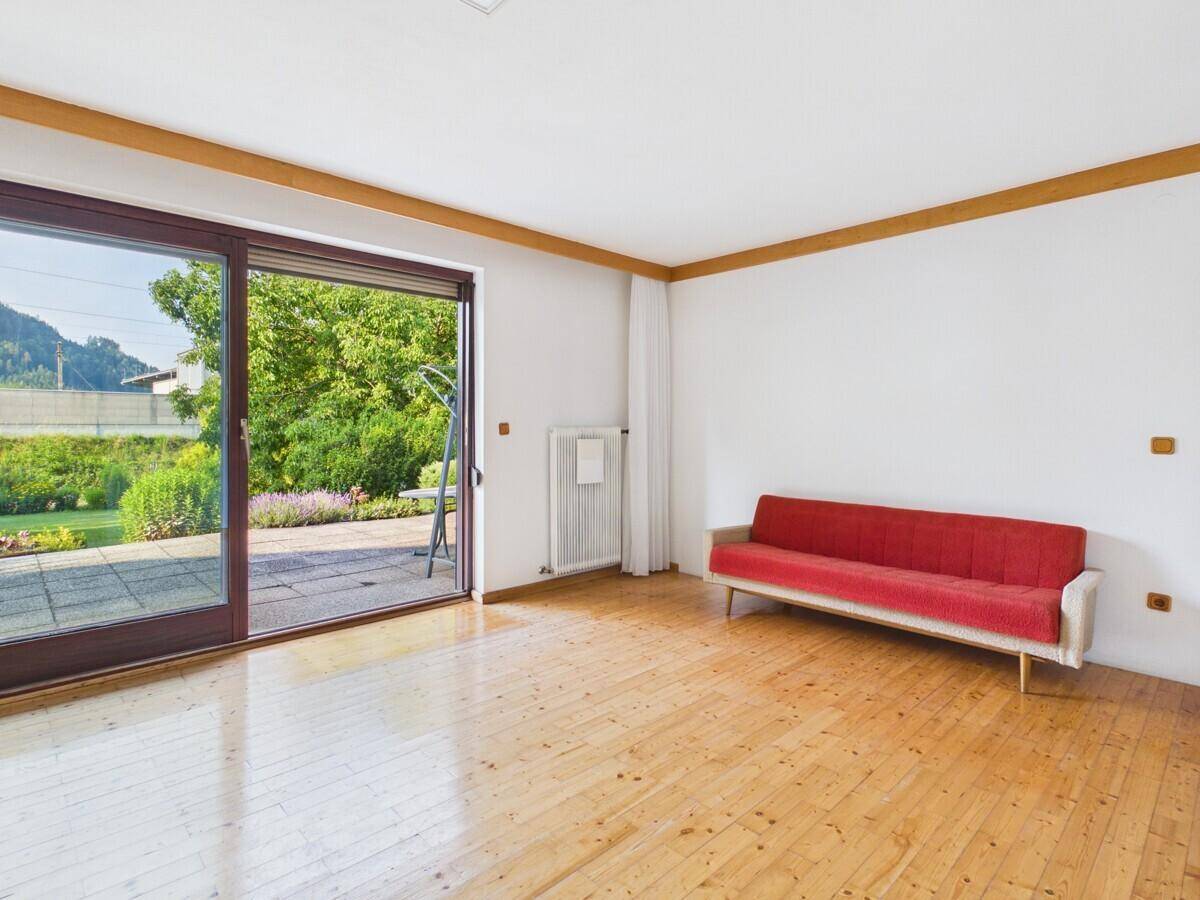 Wohnzimmer mit Holzboden und großer Schiebetür, die Zugang zur Terrasse und zum Garten bietet.