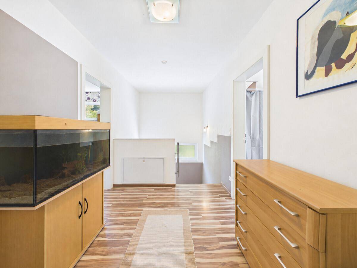 Geräumiger Flur mit Holzkommode, Aquarium und Blick auf das Treppenhaus.