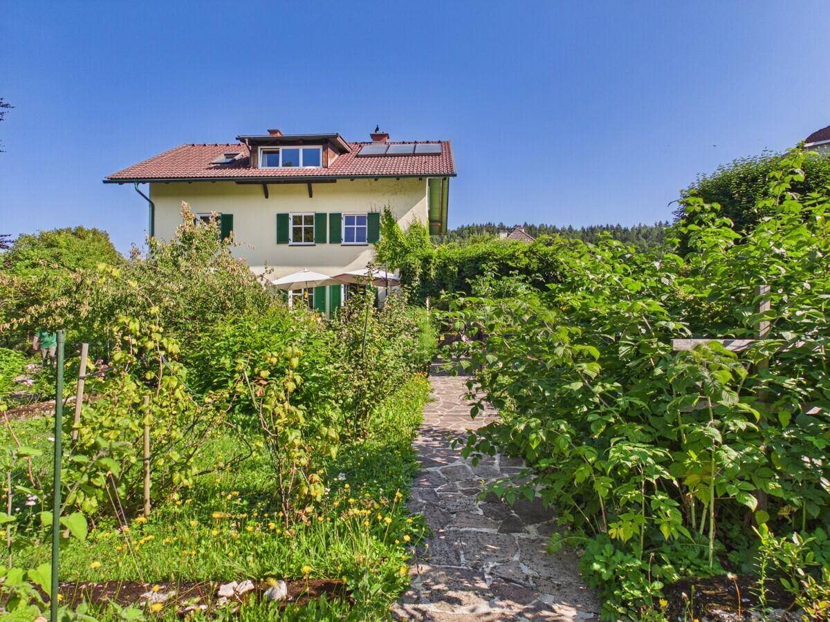Gartenweg mit üppiger Bepflanzung und Blick auf die Hausfassade mit grünen Fensterläden.