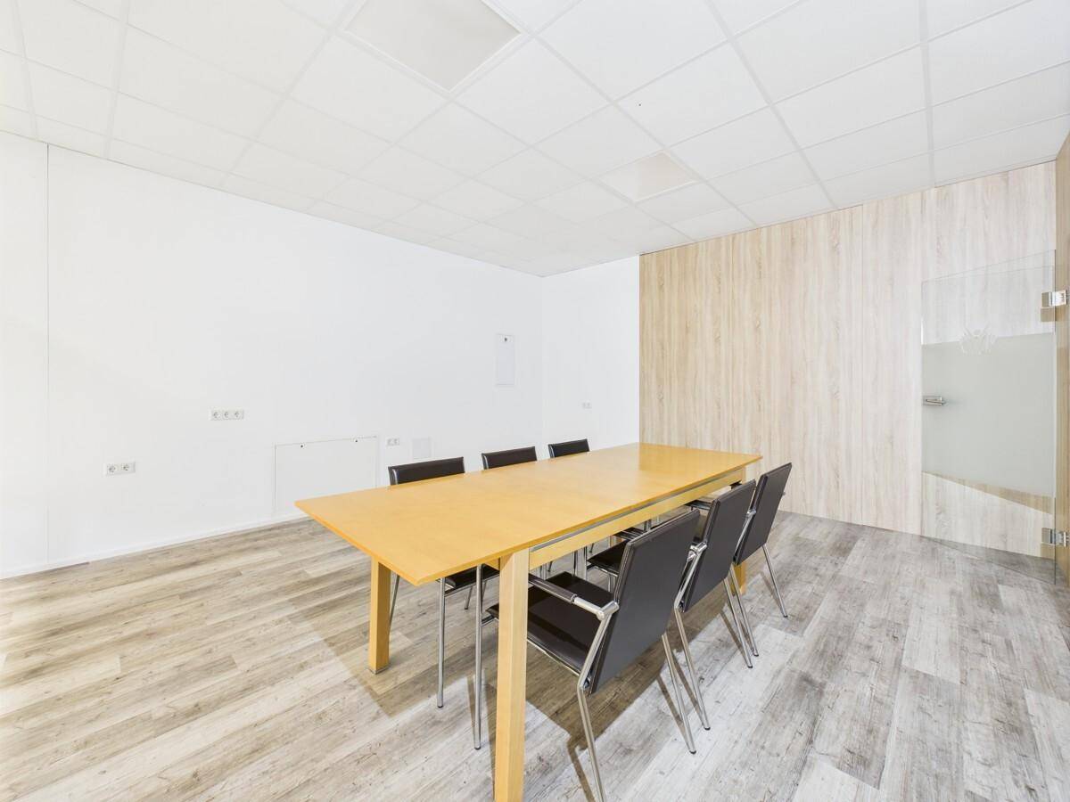 Konferenzraum mit großem Holztisch und Stühlen, hellem Laminatboden und Holzwand.