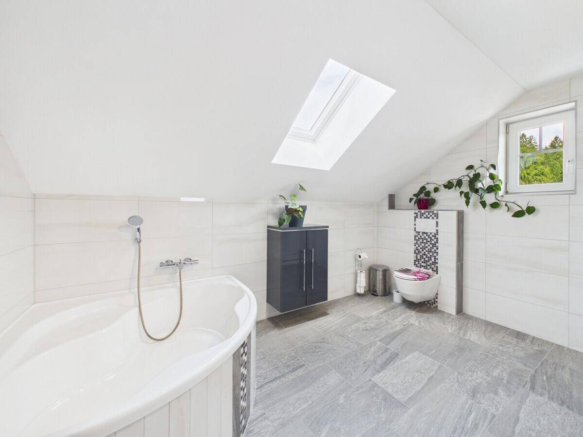 Helles Dachgeschossbad mit Badewanne, Dachfenster und modernen Fliesen.