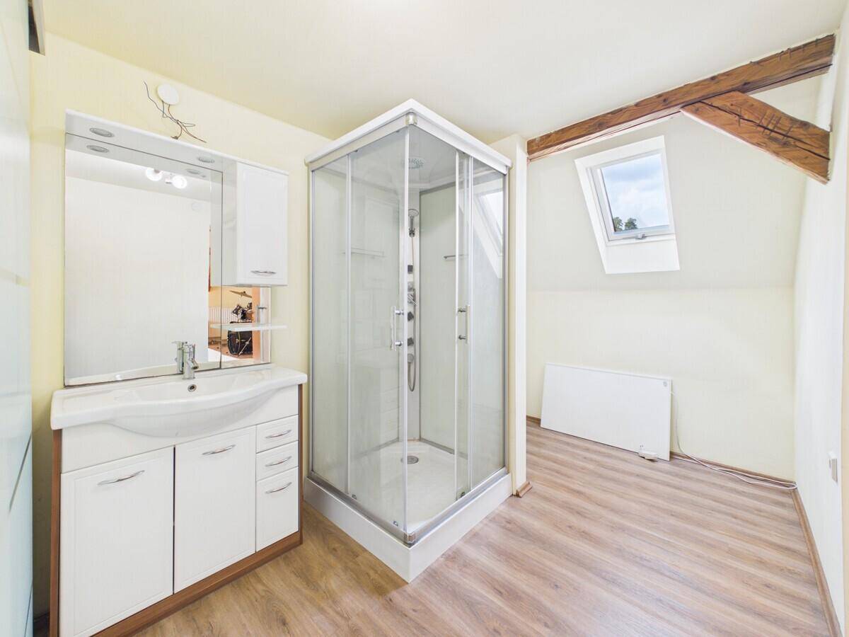 Helles Badezimmer im Dachgeschoss mit Duschkabine, Waschbecken und Dachfenster, unter Holzbalken.