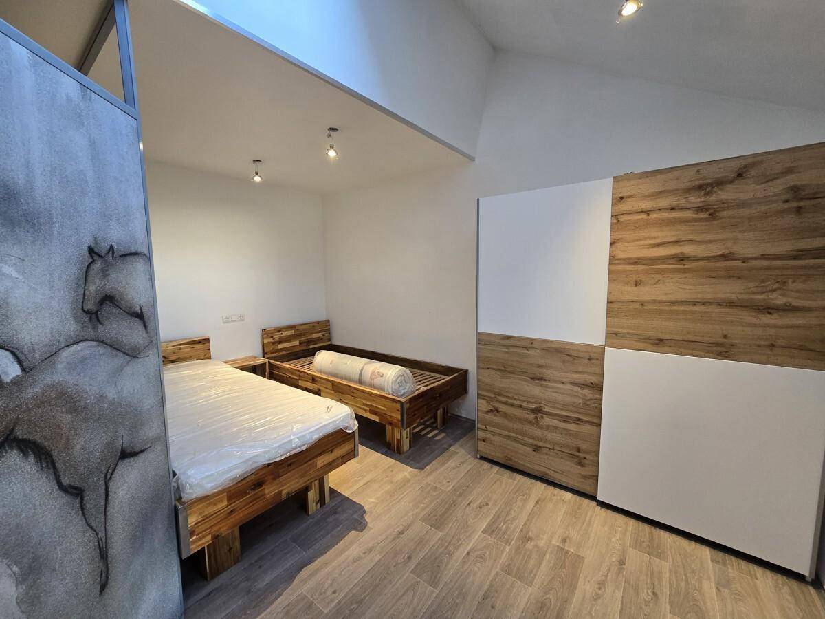 Schlafzimmer mit zwei Holzbetten, Holzboden und einem großen Dachfenster für viel Tageslicht.