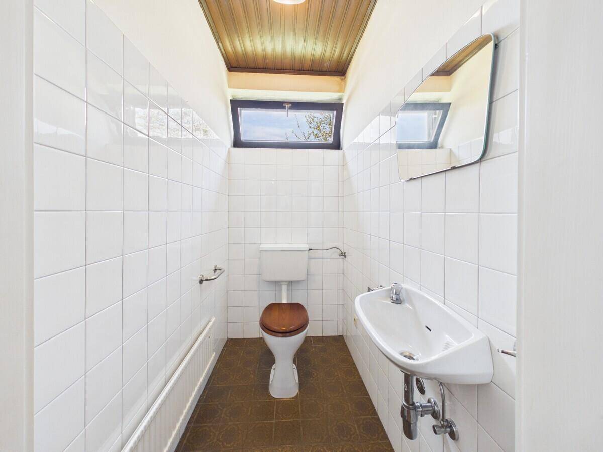 Gäste-WC mit weißen Fliesen, kleinem Waschbecken und Fenster.