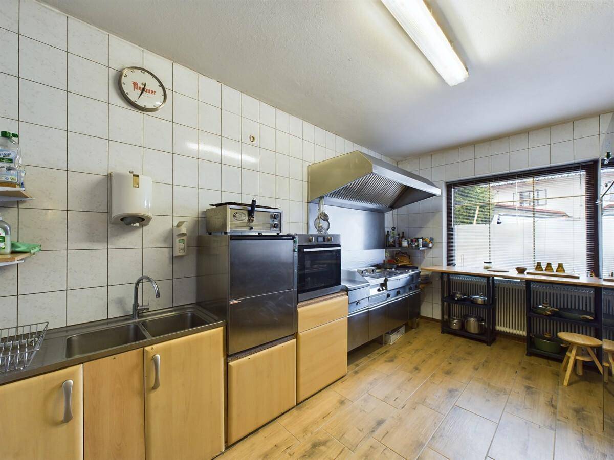 Gewerbliche Küche mit Edelstahlgeräten, Fliesenwänden und großem Fenster.