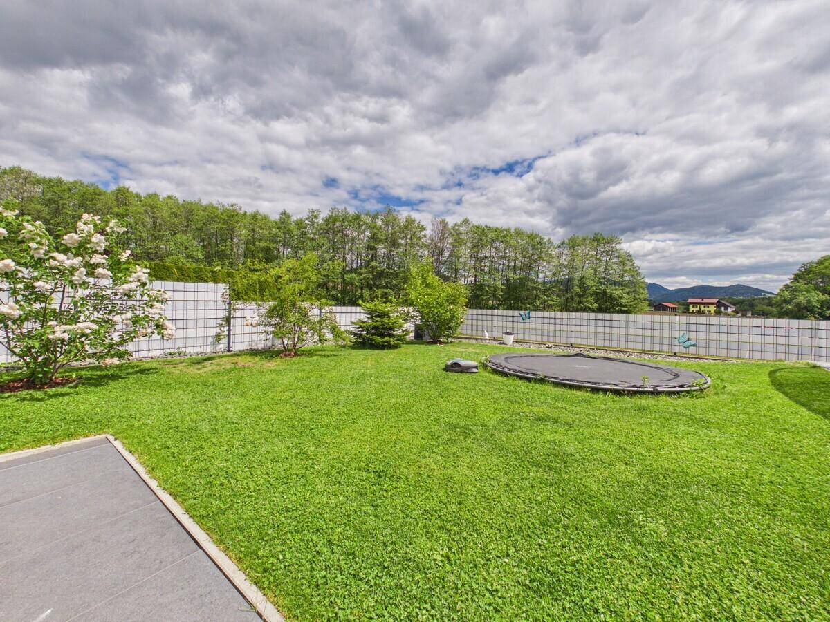 Weitläufiger Garten mit Rasenfläche, Trampolin und blühenden Sträuchern, umzäunt.