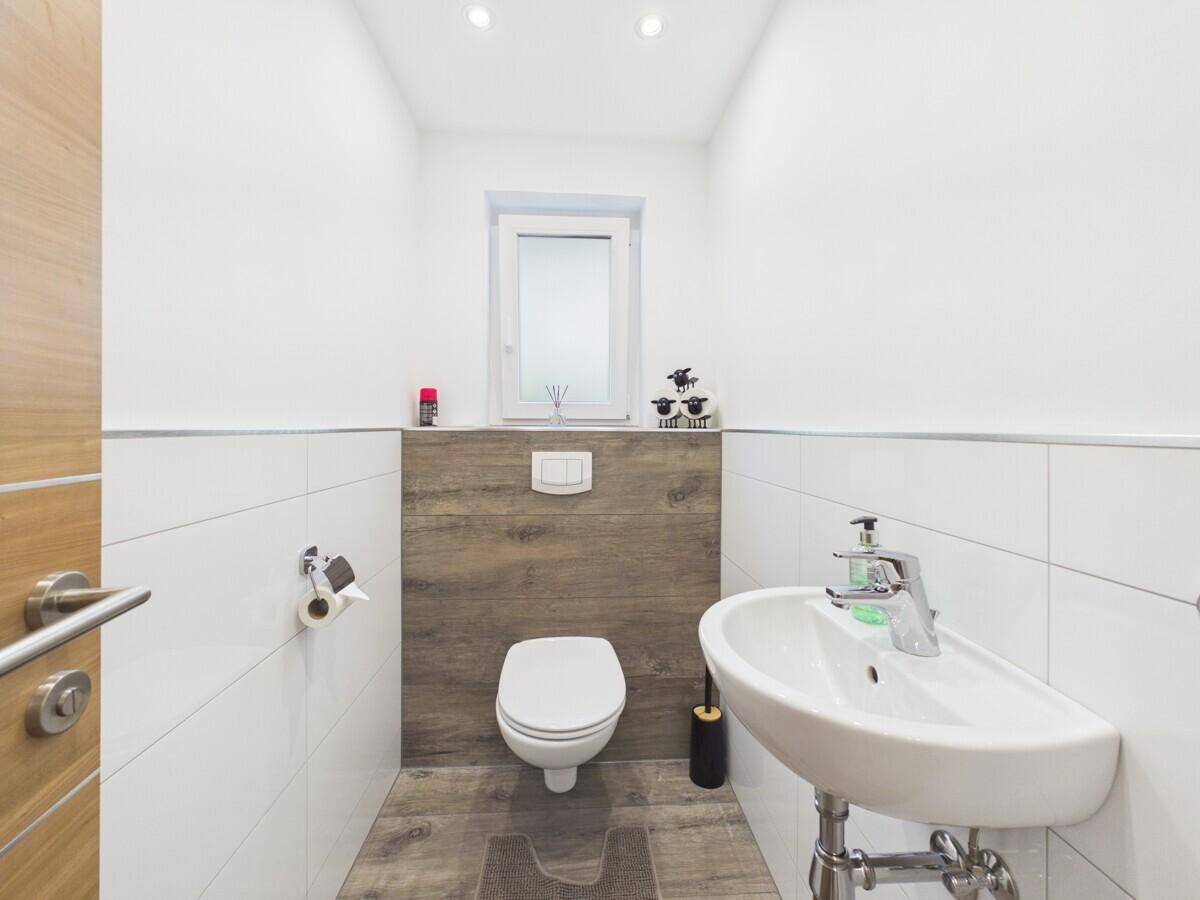 Modernes Gäste-WC mit wandhängender Toilette, kleinem Waschbecken und Fenster.