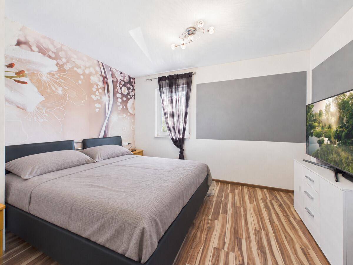 Schlafzimmer mit großem Bett, auffälliger Wandgestaltung und modernem Laminatboden.