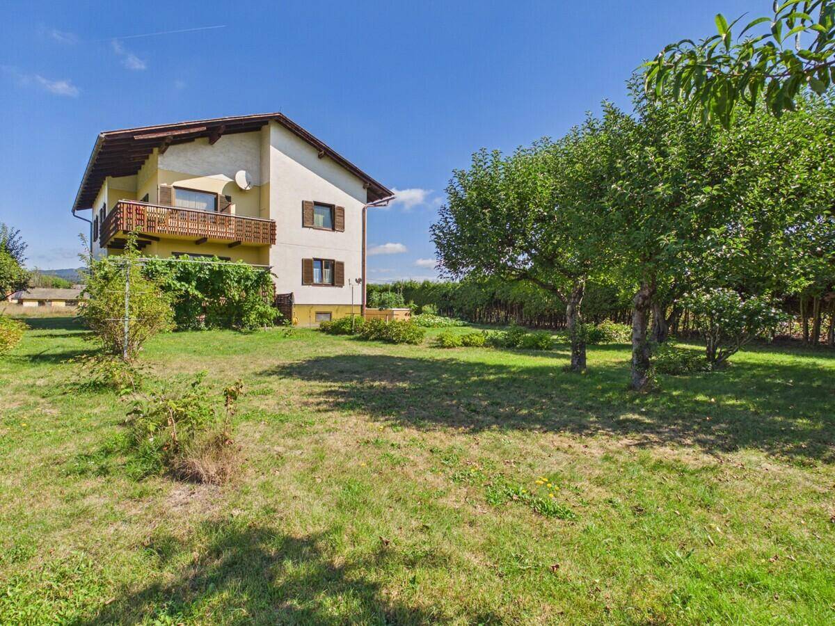 Seitenansicht des Hauses mit Balkon und einem weitläufigen Gartenbereich mit Bäumen.
