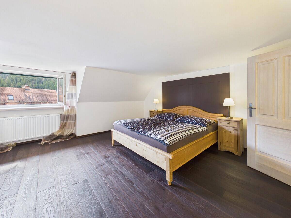 Gemütliches Schlafzimmer mit Holzbett, dunklem Holzboden und Fenster mit Bergblick.