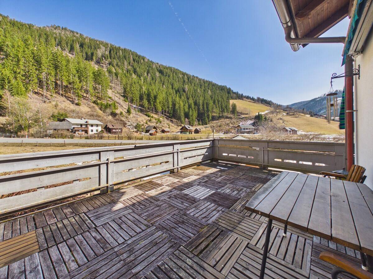 Sonniger Balkon mit Holzboden und Panoramablick auf die Alpen und das Tal.