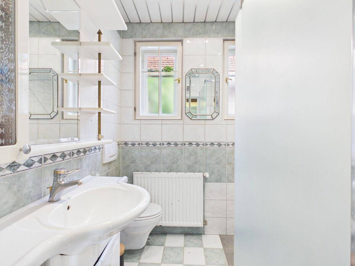 Badezimmer mit Waschbecken, Toilette, Fenster und hellen Fliesen.