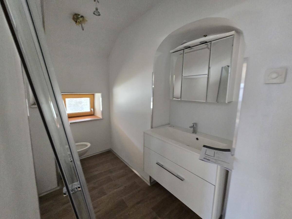 Modernes Badezimmer mit Waschtisch, Spiegelschrank und Fenster, das für natürliche Belüftung sorgt.